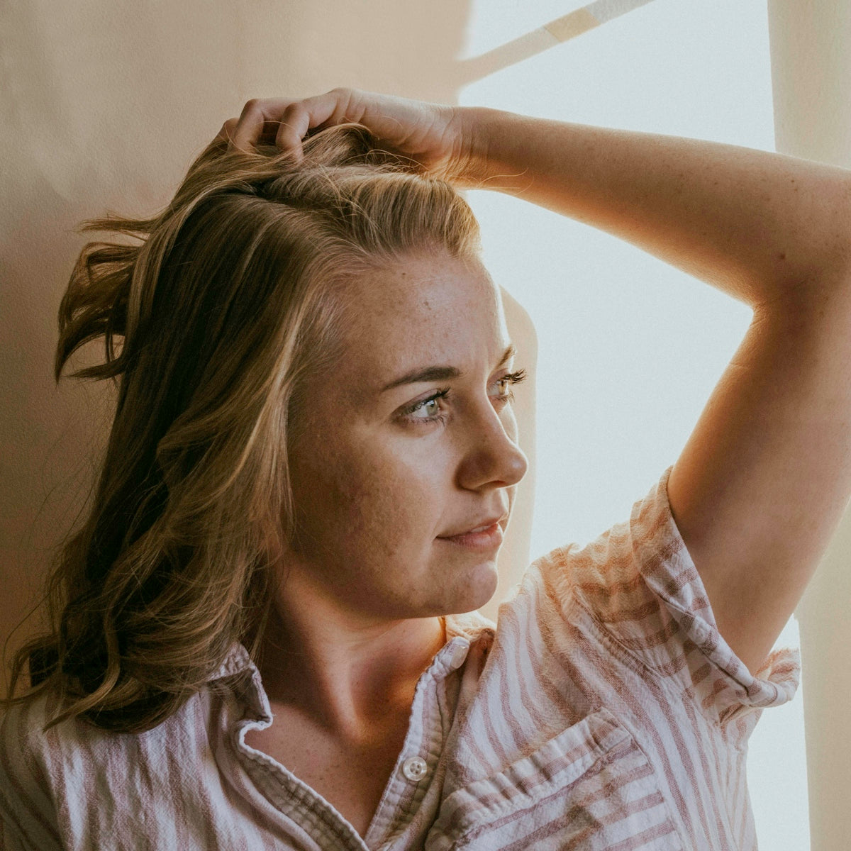 woman wearing white and brown striped collared blouse facing her left side while putting left hand on head