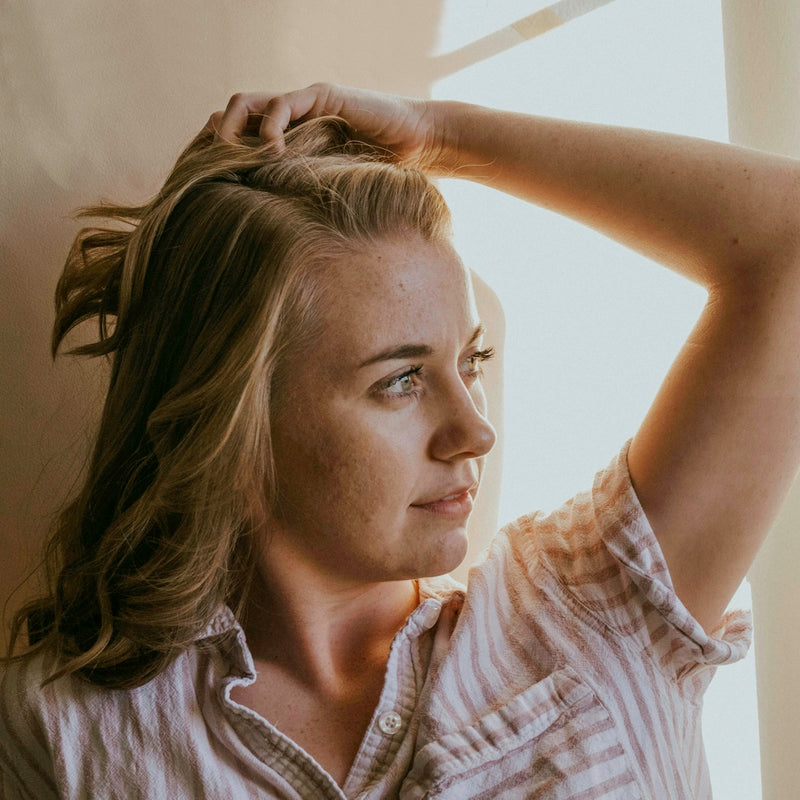 woman wearing white and brown striped collared blouse facing her left side while putting left hand on head